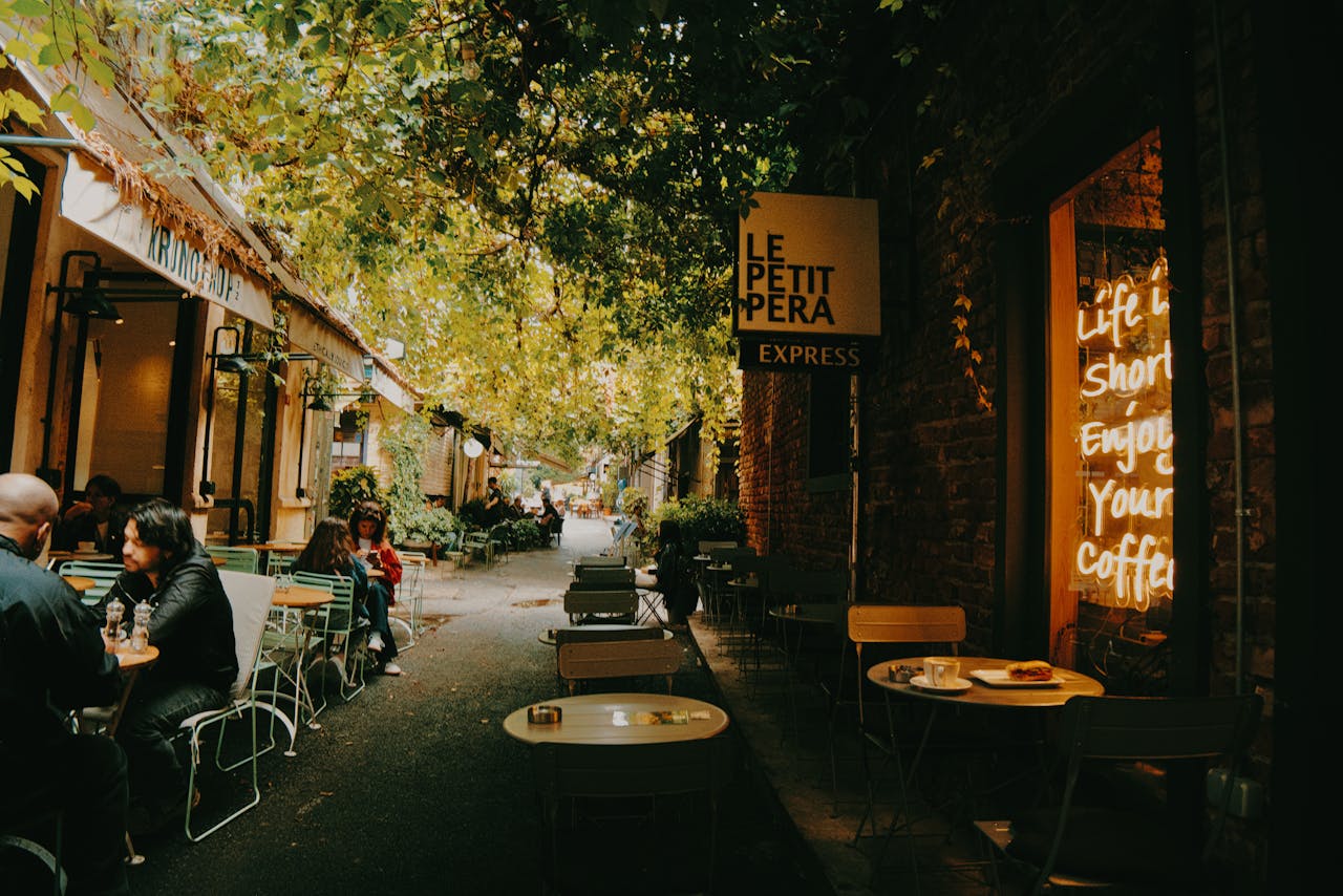 A cozy outdoor café scene with people enjoying coffee under trees in a charming alleyway.